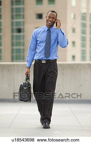 USA, Utah, Salt Lake City, Young businessman walking and talking on mobile phone View Large Photo Image Stock Photo - USA, Utah, Salt Lake City, Young businessman walking and talking on mobile phone. Fotosearch