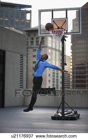 Stock Photo - USA, Utah, Salt Lake City, Young businessman scoring basketball goal. Fotosearch