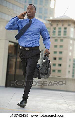 USA, Utah, Salt Lake City, Young businessman running and talking on mobile phone View Large Photo Image Stock Photography - USA, Utah, Salt Lake City, Young businessman running and talking on mobile phone. Fotosearch
