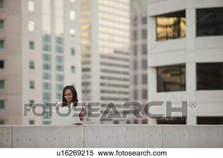 Stock Photography - USA, Utah, Salt Lake City, Young businesswoman using laptop in front of skyscrapers. Fotosearch