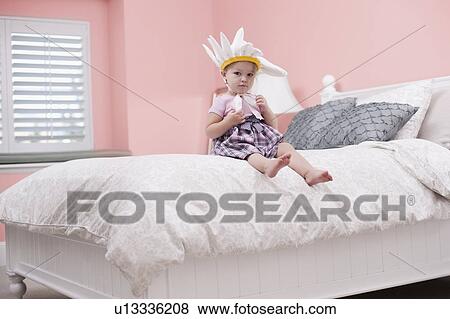 Stock Photo - USA, Utah, small girl (2-3) with plume sitting on bed. Fotosearch