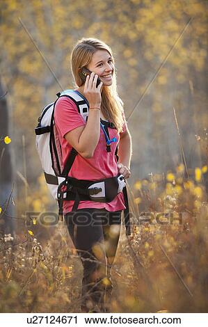 Stock Image - USA, Utah, young woman hiking in forest and talking on mobile phone. Fotosearch