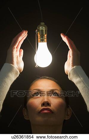 Picture - Woman looking up at illuminated lightbulb. Fotosearch