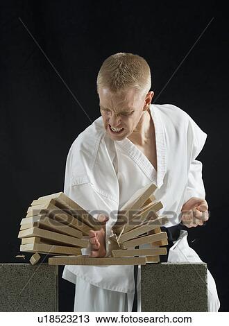 Stock Image - Young man breaking boards with karate chop on black background. Fotosearch