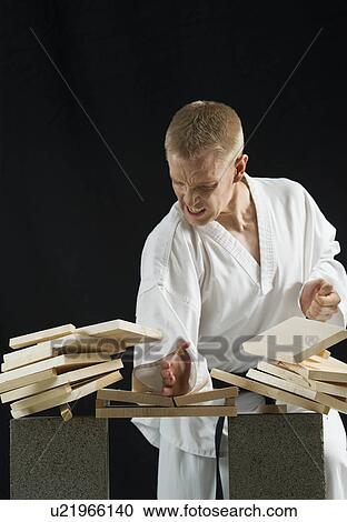 Stock Image - Young man breaking boards with karate chop on black background. Fotosearch