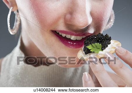 Picture - Young woman eating caviar on biscuit. Fotosearch