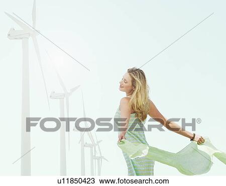 Stock Image - Young woman standing near wind turbines. Fotosearch