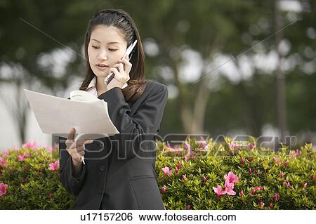 Stock Photograph - Businesswoman Reading Document Over Phone. Fotosearch