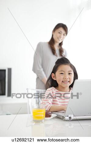 Stock Image - Girl using laptop and mother watching her. Fotosearch