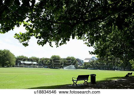 Stock Photograph - Park Bench Tree Lawn Sprinkler Water. Fotosearch