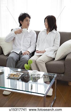 Stock Image - Young couple relaxing on sofa drinking coffee. Fotosearch