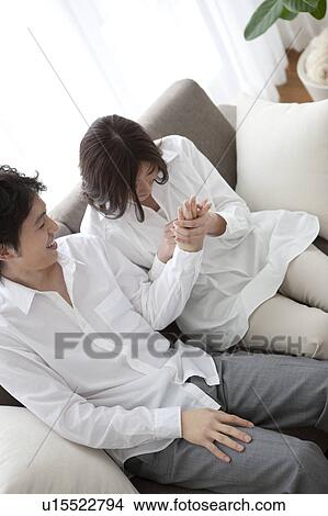 Picture - Young couple relaxing on sofa holding hands. Fotosearch