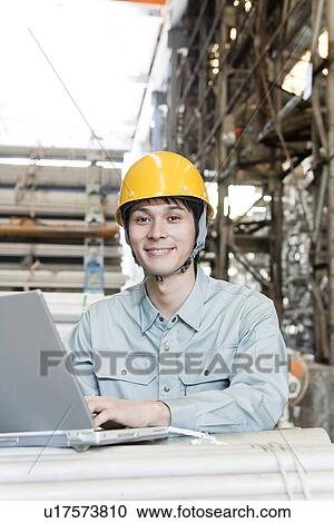 Stock Image - Young Warehouseworker Using Laptop. Fotosearch