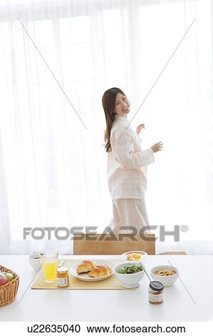Stock Image - Young woman in pajamas and breakfast on table. Fotosearch
