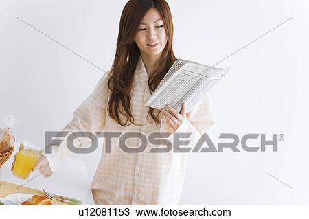 Stock Image - Young woman in pajamas holding a glass of orange juice. Fotosearch