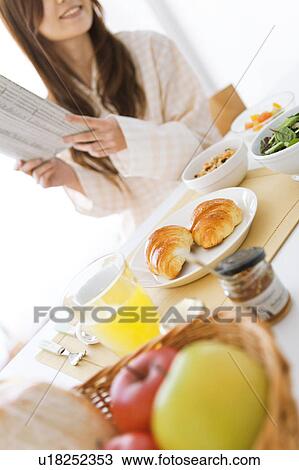 Stock Image - Young woman in pajamas reading a newspaper. Fotosearch