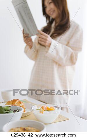 Stock Image - Young woman in pajamas reading a newspaper. Fotosearch