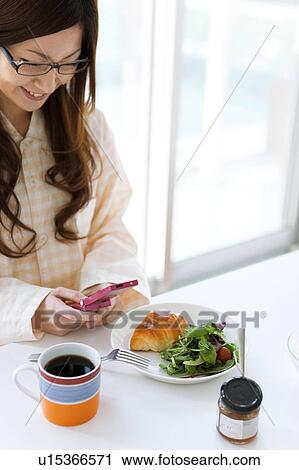Young woman in pajamas sitting at table and using cell phone View Large Photo Image Stock Image - Young woman in pajamas sitting at table and using cell phone. Fotosearch