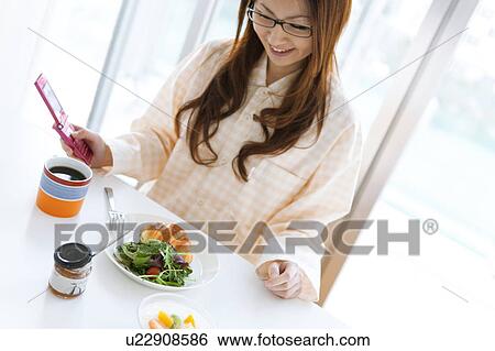 Stock Photograph - Young woman in pajamas sitting at table and using cell phone. Fotosearch