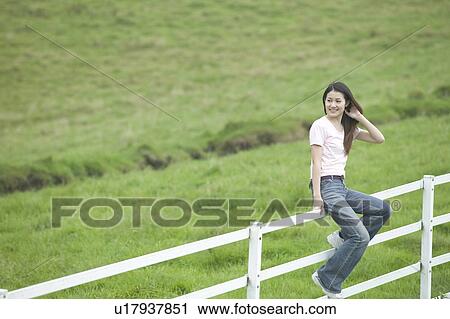 Stock Image - Young Woman Sitting on Fence. Fotosearch