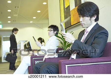 Stock Image - Businessman waiting at reception area checking his mobile phone. Fotosearch
