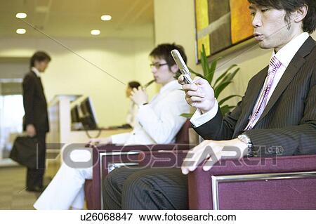 Businessman waiting at reception area checking his mobile phone View Large Photo Image Stock Photo - Businessman waiting at reception area checking his mobile phone. Fotosearch