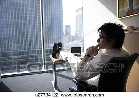 Stock Image - Businessman with feet up on desk. Fotosearch