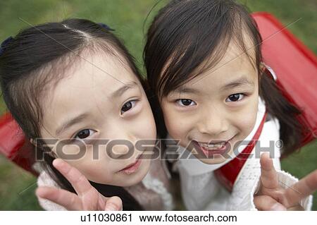 Stock Image - Elementary schoolgirls looking at camera making peace signs. Fotosearch