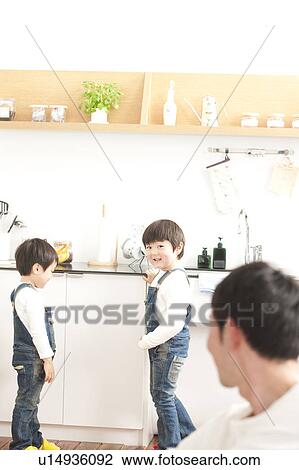 Stock Image - Father looking at sons in the kitchen. Fotosearch