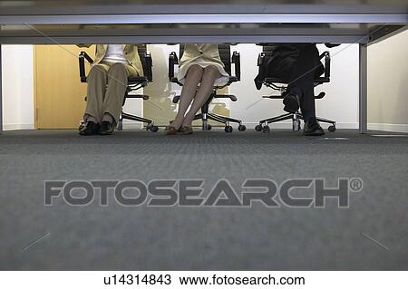 Stock Image - Legs of businesspeople having a meeting. Fotosearch