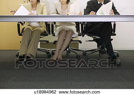 Stock Image - Legs of businesspeople having a meeting. Fotosearch