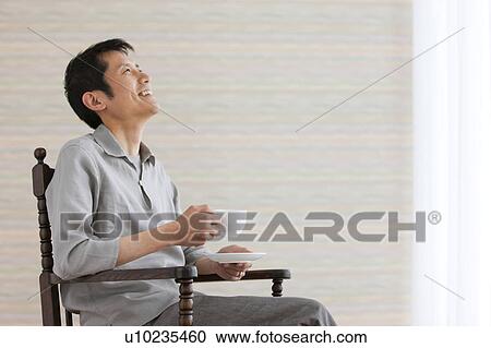 Stock Image - Man with legs crossed at knee holding coffee. Fotosearch