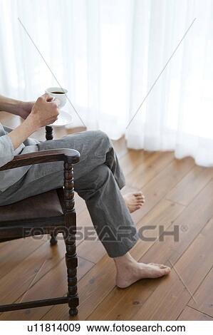 Stock Photo - Man with legs crossed at knee holding coffee. Fotosearch