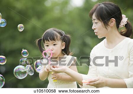 Stock Photo - Mother helping daughter blowing bubbles. Fotosearch