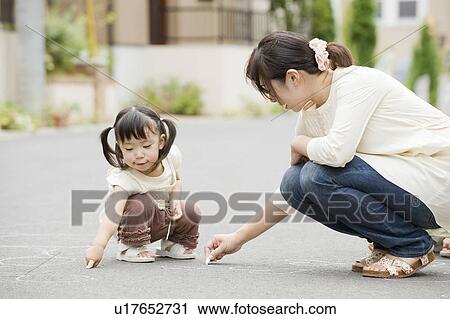 Stock Image - Mother writing on street with chalk. Fotosearch
