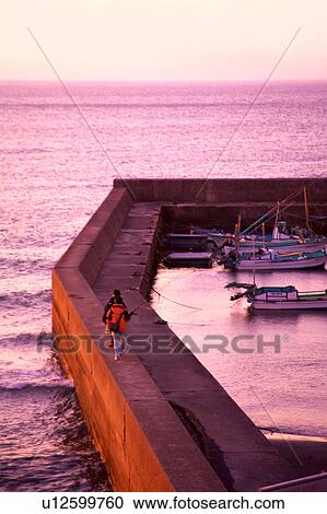 Stock Image - Person Walking on Flood Defence. Fotosearch
