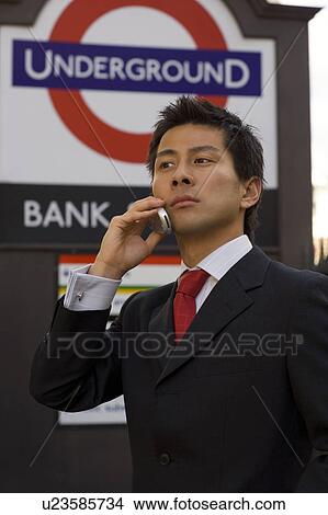 Picture - The businessman who applies a cellular phone at the subway entrance in London. Fotosearch
