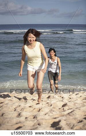 Stock Image - Young couple running on beach, Guam, USA. Fotosearch