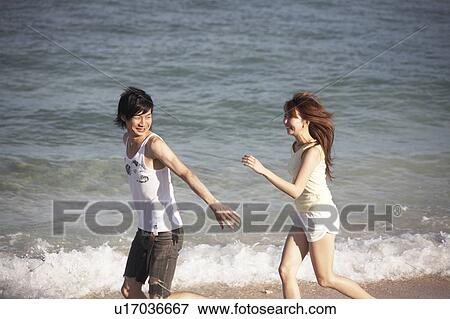 Stock Photo - Young couple running on beach, Guam, USA. Fotosearch