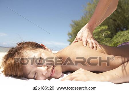 Stock Image - Young woman getting a back massage on beach. Fotosearch