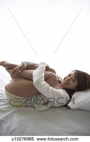 Stock Photograph - Young woman hugging knees on bed. Fotosearch