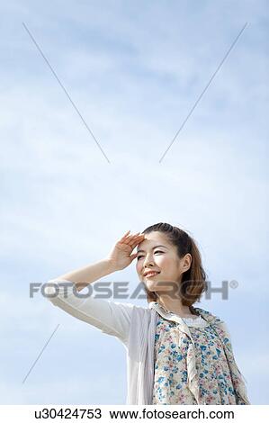Stock Image - Young woman looking at sun. Fotosearch