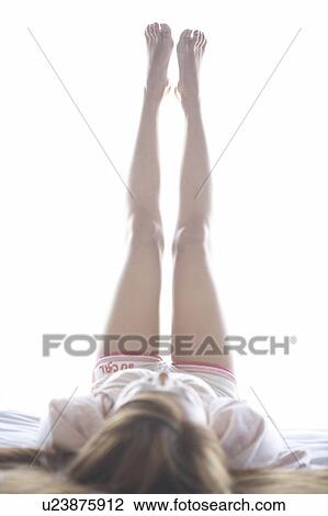 Stock Image - Young woman lying on back with legs up. Fotosearch