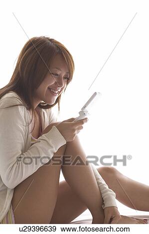 Stock Photo - Young woman sitting on bed text messaging. Fotosearch