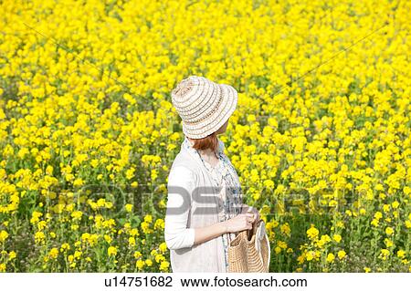 Stock Image - Young woman standing next to oilseed rape field. Fotosearch