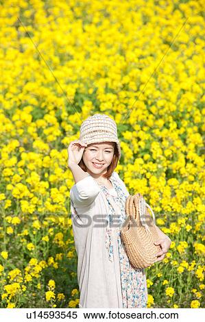 Stock Photography - Young woman standing next to oilseed rape field. Fotosearch
