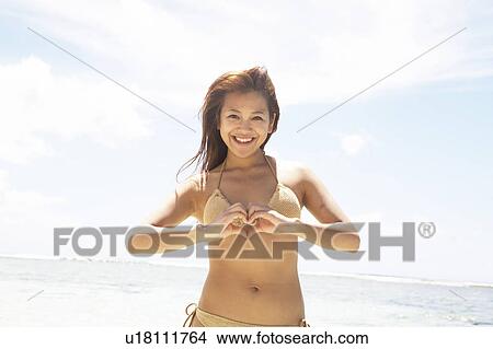 Picture - Young woman standing on beach making heart with hands, Guam, USA. Fotosearch