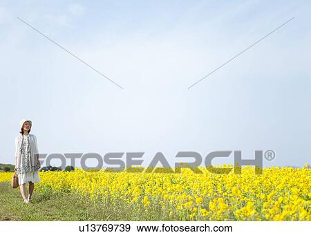 Stock Photo - Young woman walking next to oilseed rape field. Fotosearch