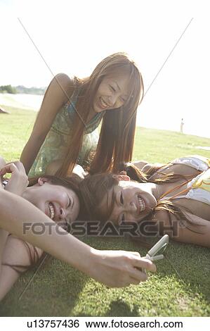 Young women lying on grass looking at cell phone, Guam, USA View Large Photo Image Stock Photograph - Young women lying on grass looking at cell phone, Guam, USA. Fotosearch