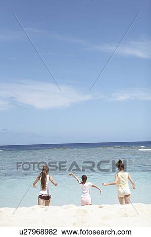 Stock Image - Young women running on beach, Guam, USA. Fotosearch